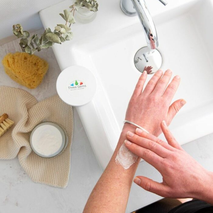 A lady using the Three Gems Shea Body Butter on her arm over a bathroom sink