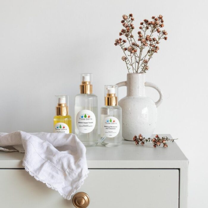 Three Gems Cleanser, Toner, and Frankincense Face Oil on a table with a dried flower arrangement