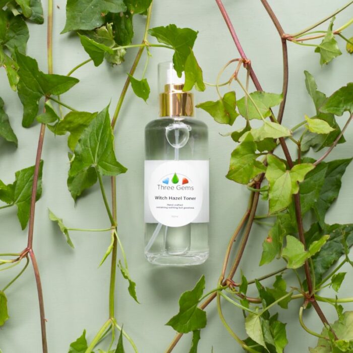 Three Gems organic Witch Hazel Toner laying on a bed of green leaves